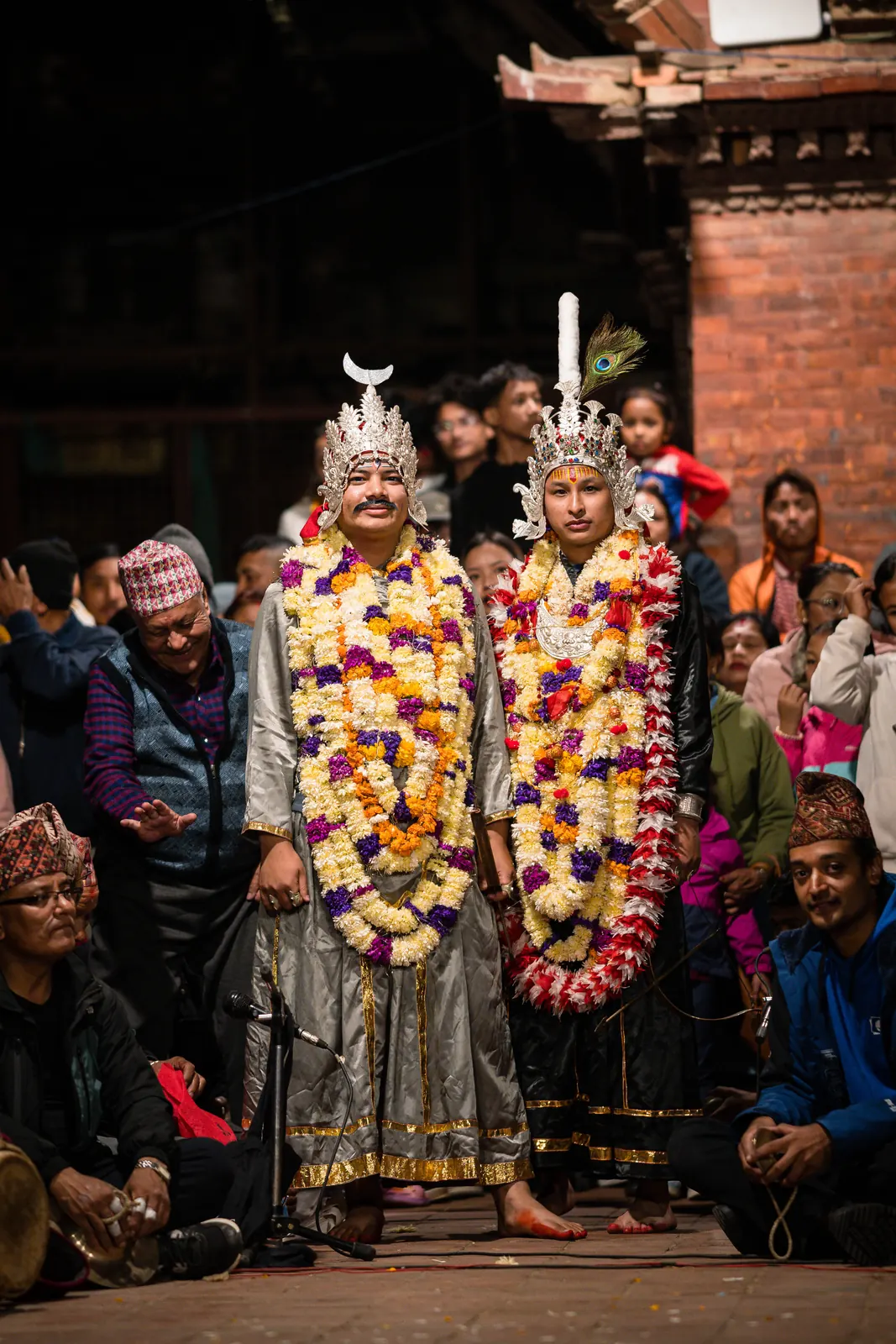 Two crowned performers in garlands stand side by side